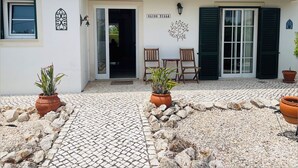 Un edificio con techo de tejas, un cartel que dice "BLOSS VILLA", dos sillas de madera y plantas en macetas.