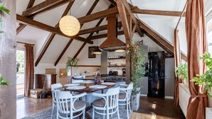 Un comedor amplio con techo alto y vigas de madera a la vista, una isla central con asientos y una cocina al fondo.
