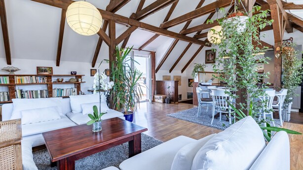 Un loft espacioso con vigas de madera a la vista, una zona de estar acogedora con un sofá y una mesa baja, y un comedor con una mesa y sillas blancas.