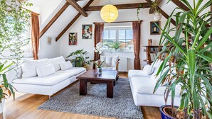 Un loft espacioso con techos altos, vigas de madera a la vista, un ventanal con cortinas y una variedad de plantas de interior.