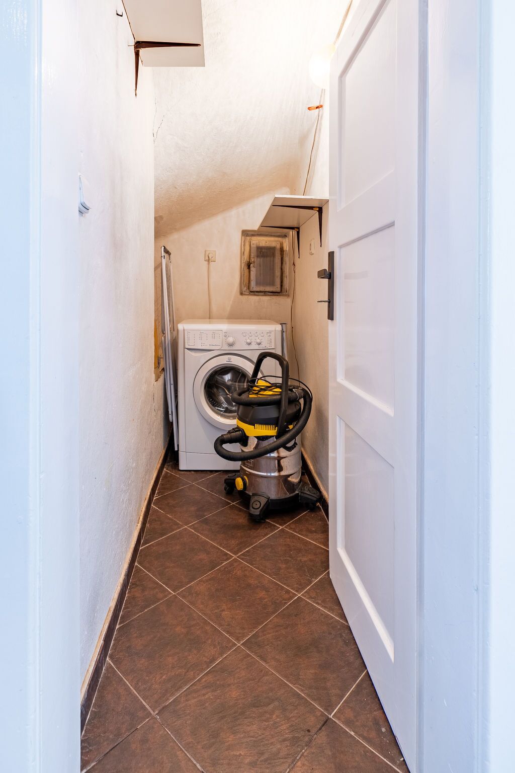 A narrow hallway with a washing machine, a vacuum cleaner, and a door.