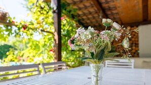 Un florero de vidrio transparente con flores sobre una mesa blanca al aire libre.