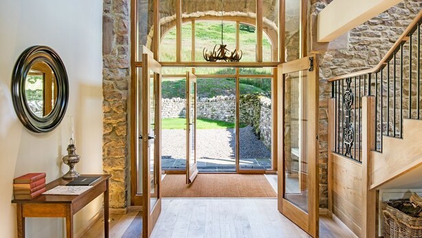 Une entrée imposante, avec un mur en pierre, un escalier en bois et une vue sur un jardin.