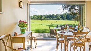 Un coin repas avec une table dressée pour six personnes, des chaises et une vue sur un champ verdoyant, visible à travers une porte vitrée.
