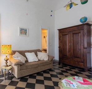 Une pièce avec un sol à carreaux, un meuble en bois, un canapé avec des coussins, une lampe et un globe posé sur le dessus du meuble.