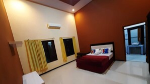 A hotel room with a bed, a bedside table, an air conditioning unit, and a window with curtains. - 999 KHS 2 Homestay (Banyuwangi)