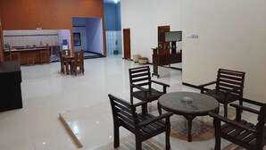 A spacious living area with a dining set, a TV stand, and a kitchen area in the background. - 999 KHS 2 Homestay (Banyuwangi)