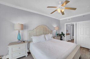 A bedroom with a bed, nightstands, a ceiling fan, a mirror, and a door. - Seawind 1401 by Liquid Life (Gulf Shores)