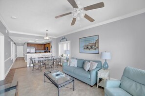 Un salon spacieux avec un canapé bleu clair, une table basse en verre et un ventilateur de plafond.