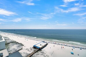 A beach with a pier extending into the ocean, a covered area with umbrellas, and a sandy beach with people and vehicles. - Seawind 1401 by Liquid Life (Gulf Shores)