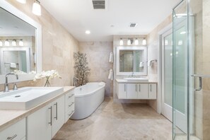 A modern bathroom with a large bathtub, a glass shower enclosure, and a vanity with a mirror. - Beachcomber 34 by Grand Cayman Villas (7 Mile Beach)