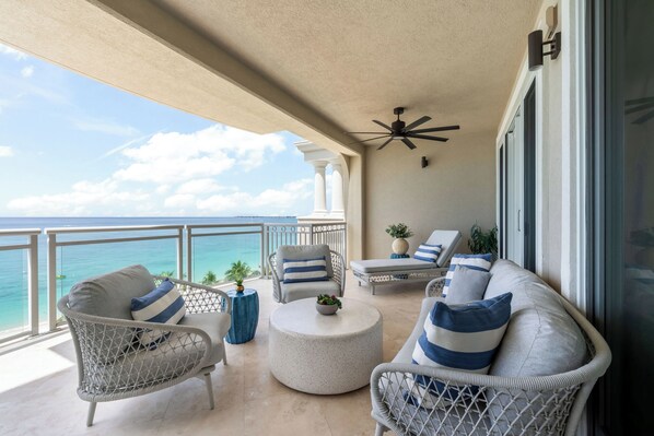 A balcony with wicker furniture, a ceiling fan, and a view of the ocean. - Beachcomber 34 by Grand Cayman Villas (7 Mile Beach)