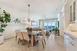 A modern kitchen with a dining area, large windows, and a view of the ocean. - Beachcomber 34 by Grand Cayman Villas (7 Mile Beach)