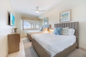 A bedroom with two beds, a ceiling fan, a window with blinds, and a framed picture on the wall. - Beachcomber 34 by Grand Cayman Villas (7 Mile Beach)