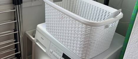 A front-loading washing machine with a white plastic basket on top, a control panel with various buttons and a digital display, and a window with a frosted glass panel.