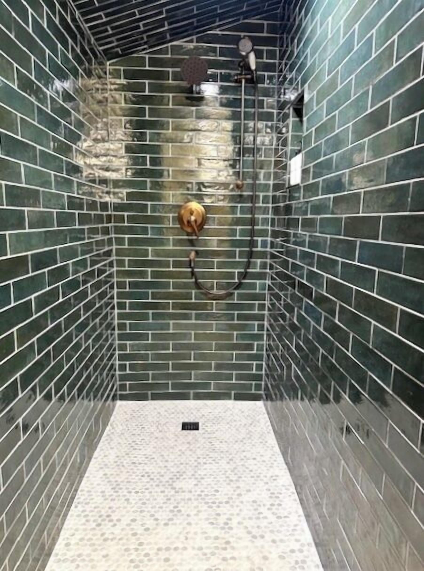 Un área de ducha con paredes de azulejos verdes y suelo de baldosas blancas.