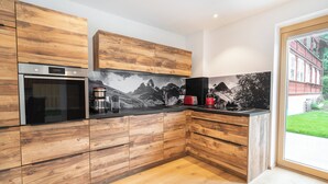 A modern kitchen with wooden cabinetry, a built-in oven, and a large window offering a view of a green landscape. - Central, south-facing terrace, mountain view, sauna, ski locker, free summer cable car (Oberstdorf)