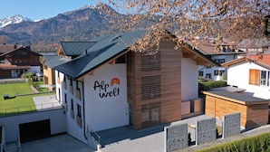 A modern building with a sloped roof, a sign reading "Alpwelt," and a view of mountains in the background. - Central, south-facing terrace, mountain view, sauna, ski locker, free summer cable car (Oberstdorf)