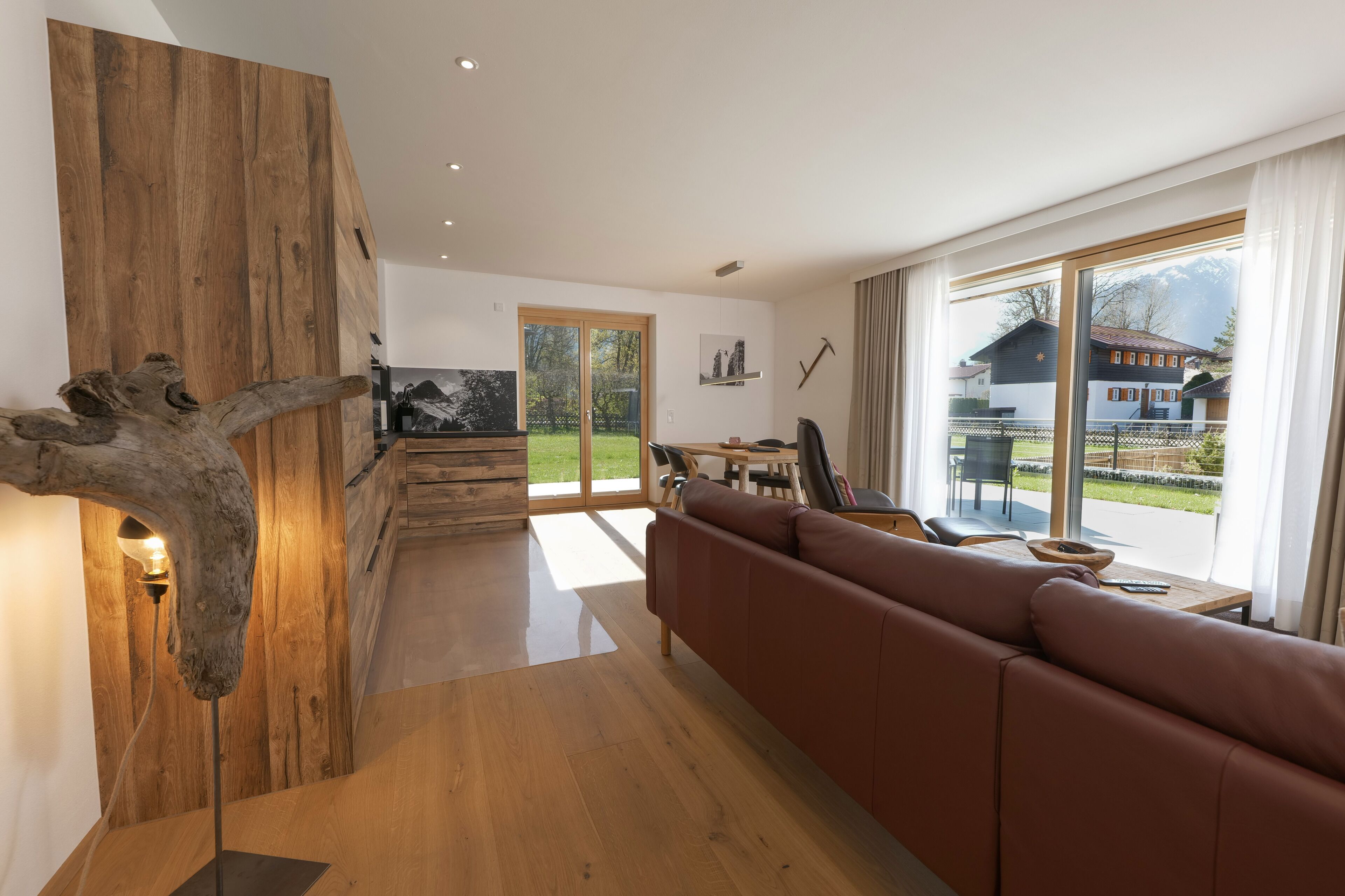 A modern living room with a wooden accent wall, a brown leather sofa, and a dining area with a view of a mountain.