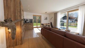 A modern living room with a wooden accent wall, a brown leather sofa, and a dining area with a view of a mountain. - Central, south-facing terrace, mountain view, sauna, ski locker, free summer cable car (Oberstdorf)