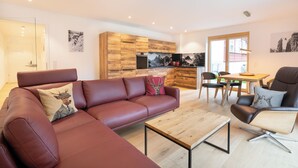 A modern living room with a leather sofa, a wooden coffee table, and a dining area with a wooden table and chairs. - Central, south-facing terrace, mountain view, sauna, ski locker, free summer cable car (Oberstdorf)
