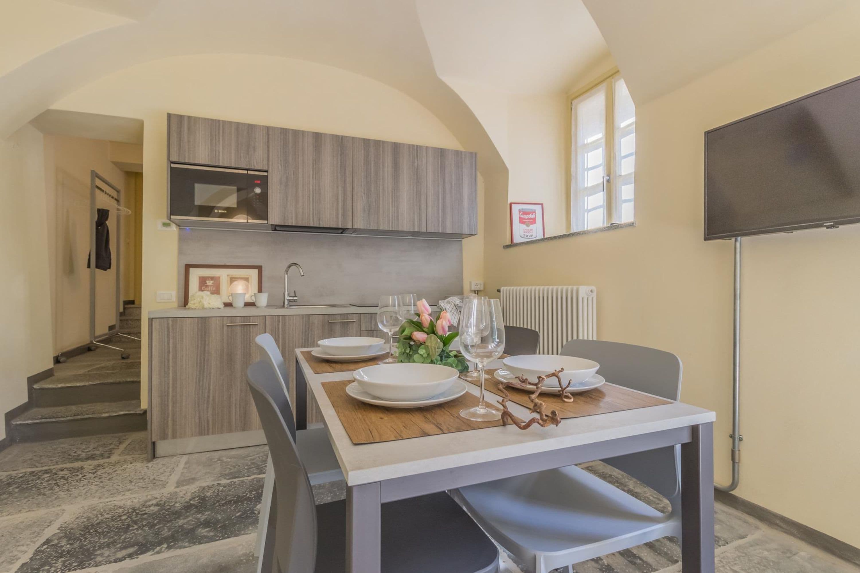 Un coin repas avec une table dressée pour deux personnes, un four à micro-ondes placé au-dessus du comptoir et un téléviseur fixé au mur.