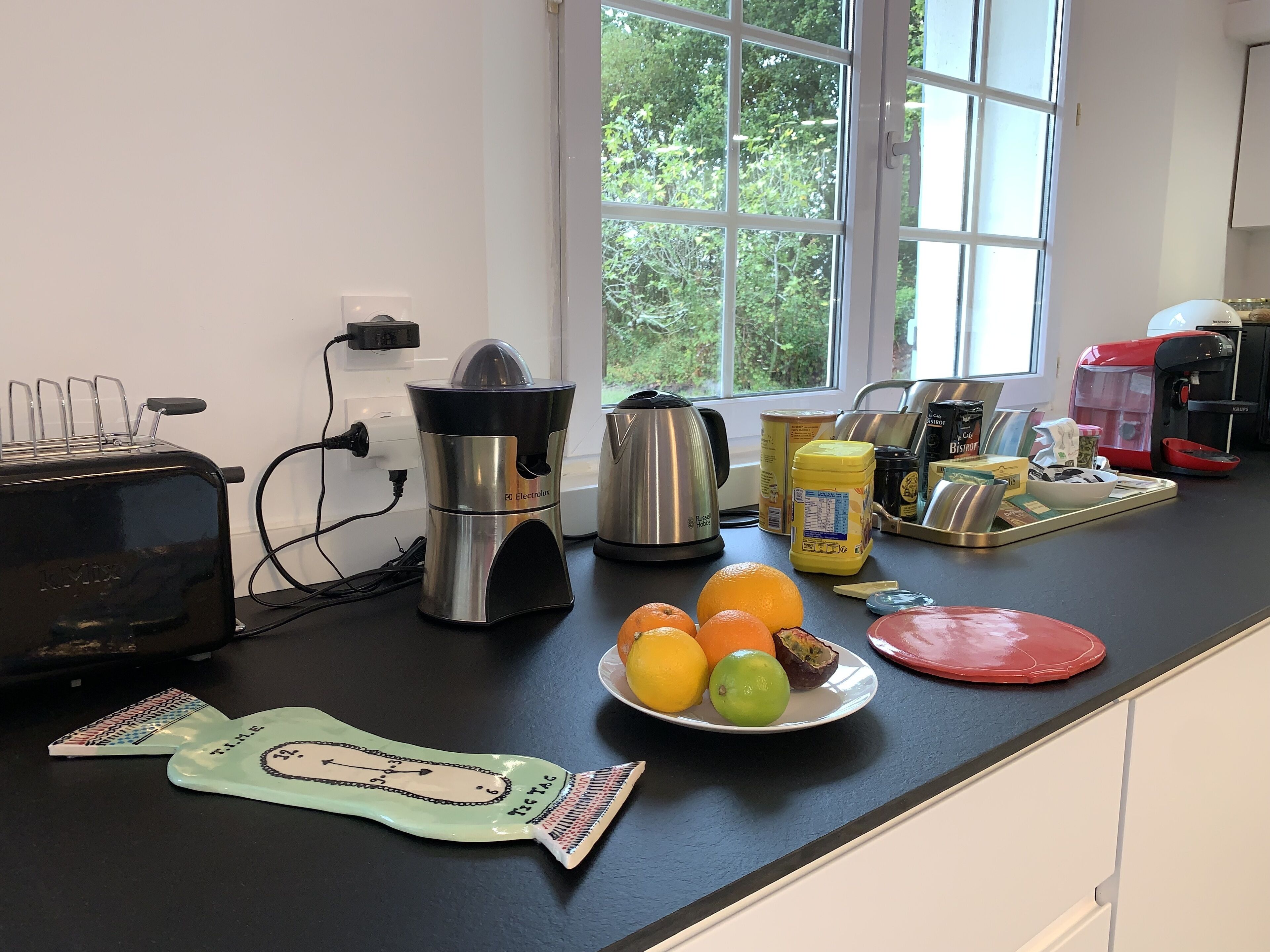 A kitchen with a toaster, coffee maker, and a window with a view of trees.