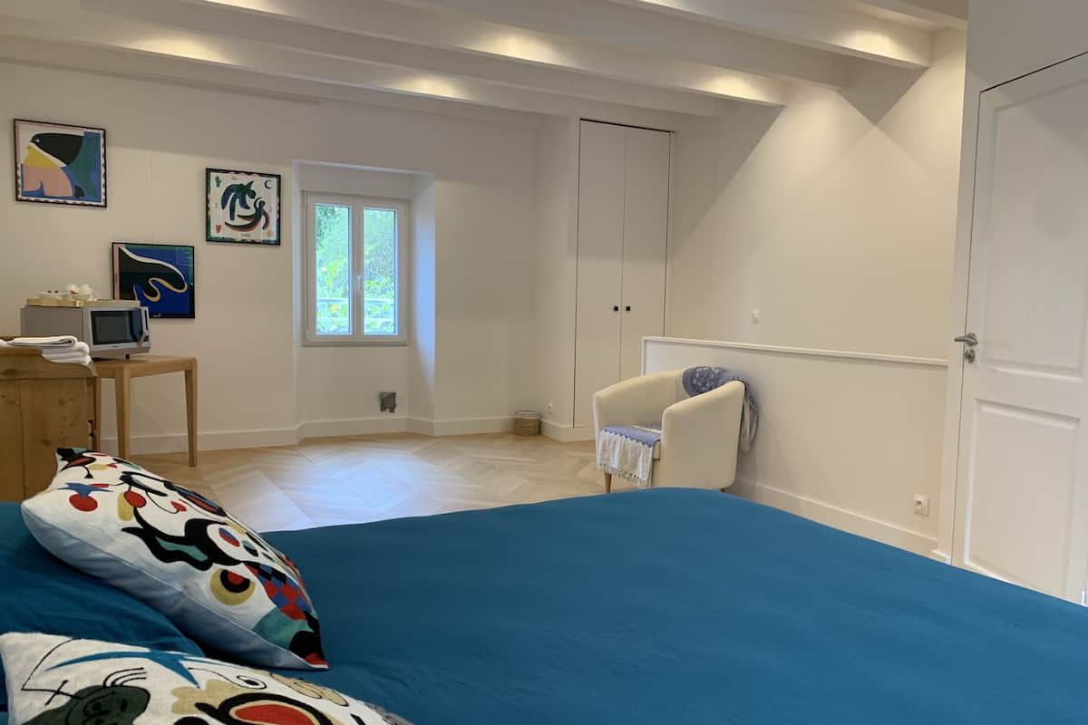 Une chambre avec un grand lit, un bureau avec un ordinateur, une chaise et une fenêtre.