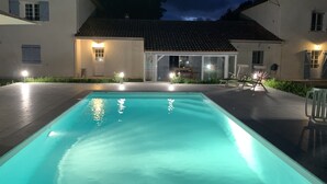 Une piscine avec une terrasse carrelée, une maison avec un toit en tuiles et une porte vitrée donnant sur un patio.