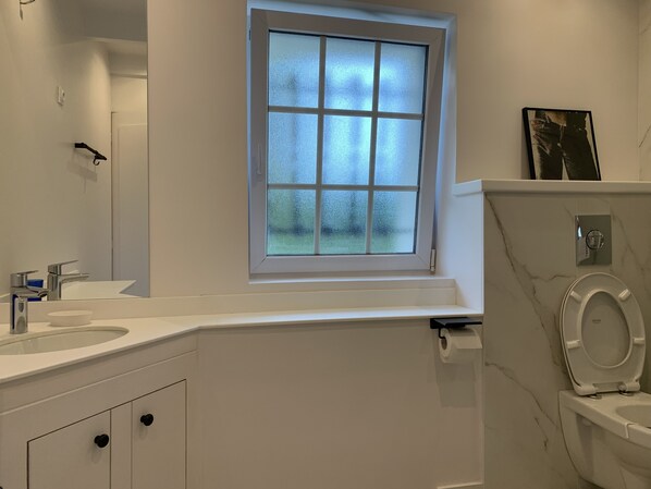 A bathroom with a white vanity, a window with frosted glass, a toilet, and a mirror.