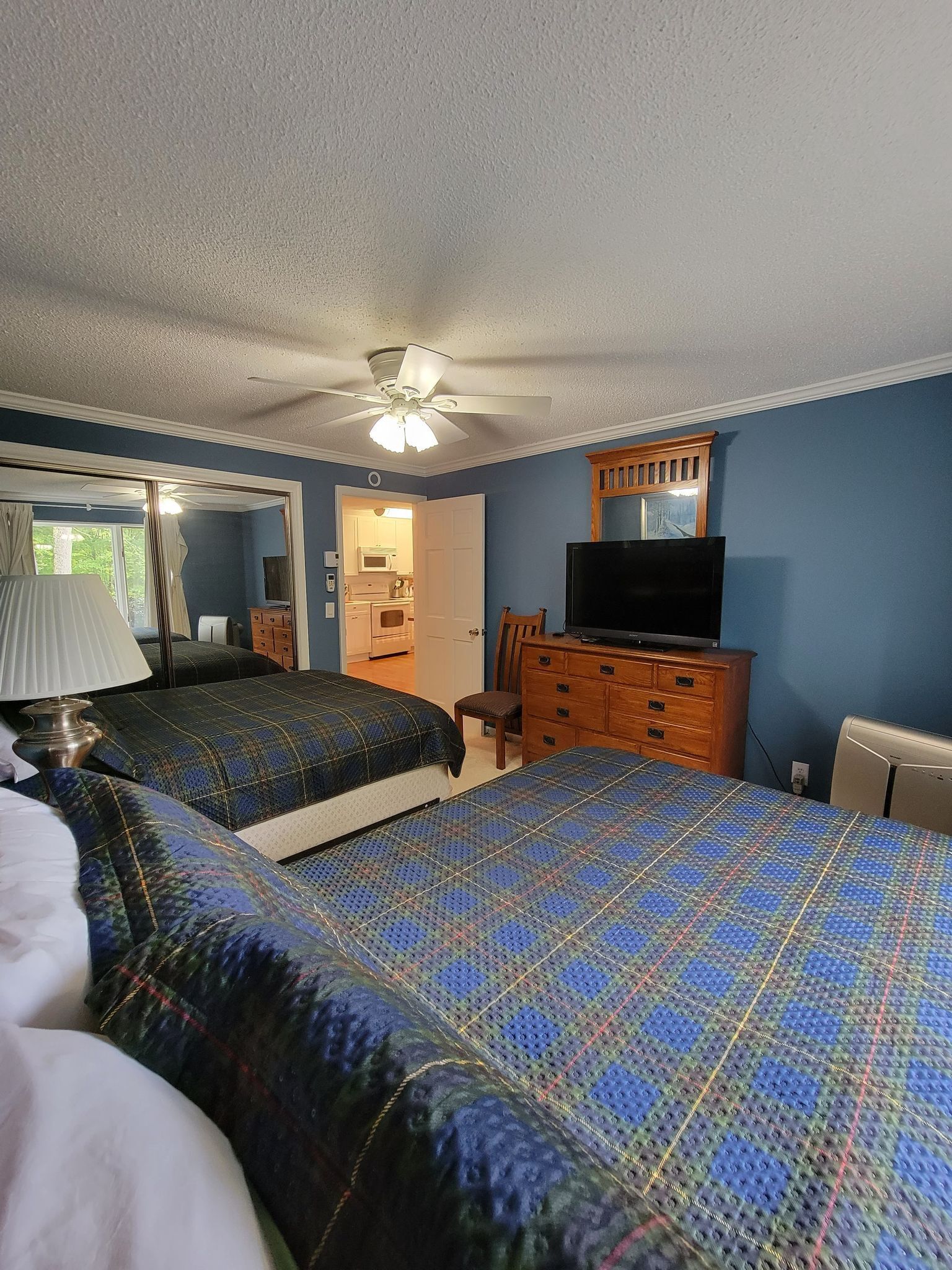 Camera d'albergo con due letti, una ventola a soffitto, una TV, un comò e vista sulla cucina.
