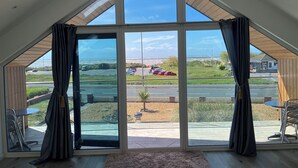 A room with large windows, a wooden ceiling, and a view of a parking lot and road. - Sea La Vie (Lytham St. Anne's)