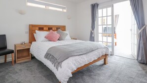 A bedroom with a wooden bed, a nightstand, a chair, and a large window with curtains. - Sea La Vie (Lytham St. Anne's)