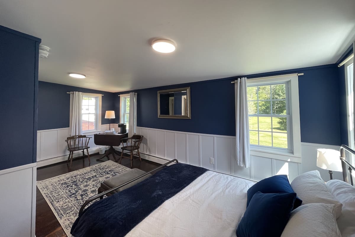 A bedroom with a bed, a desk, and two windows.