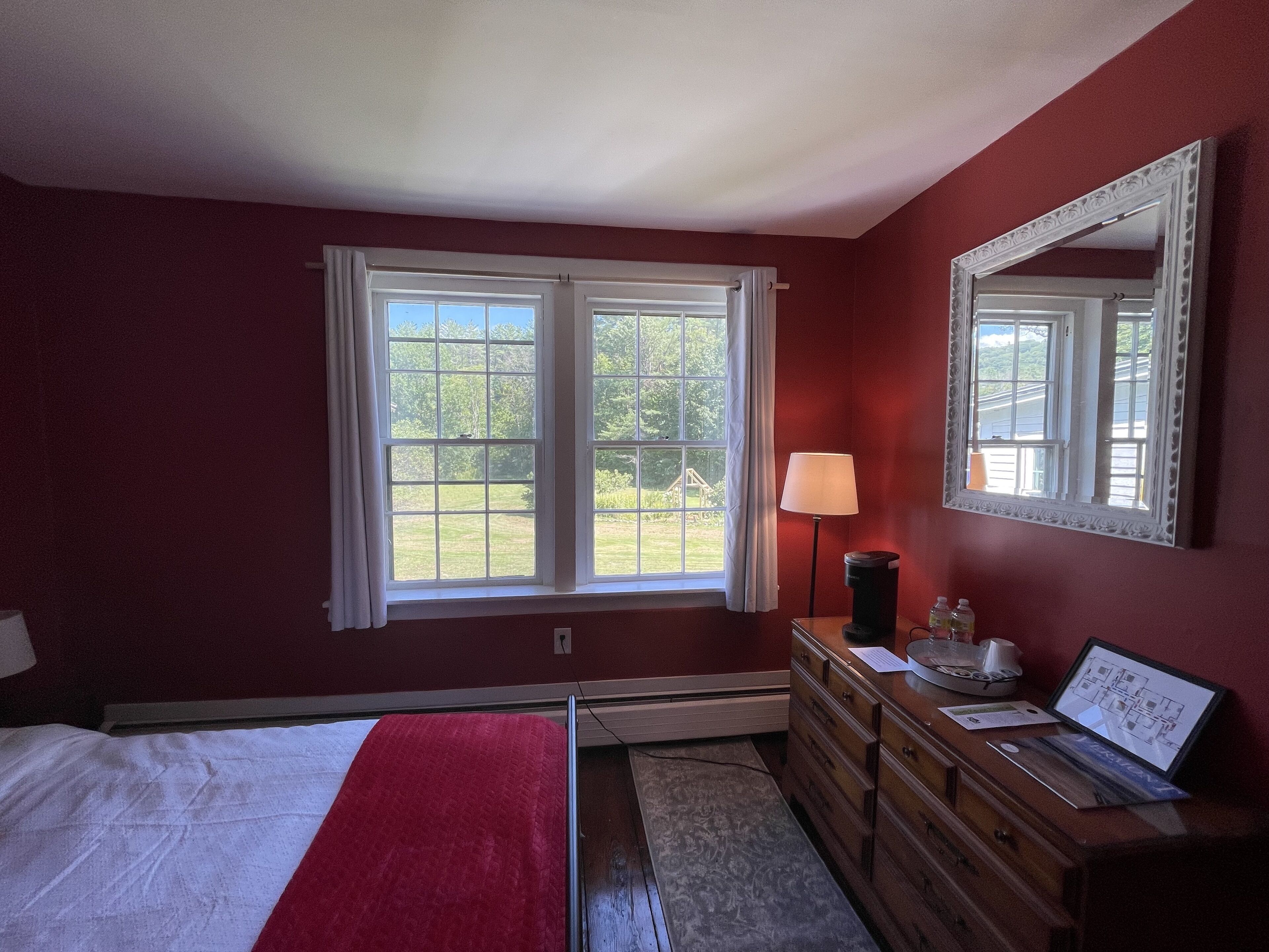 A bedroom with a bed, dresser, lamp, and a large mirror.