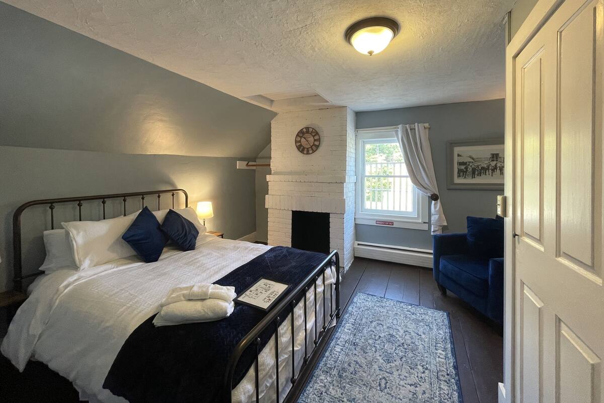 A bedroom with a bed, bedside lamp, clock, and a view of the outside through a window.