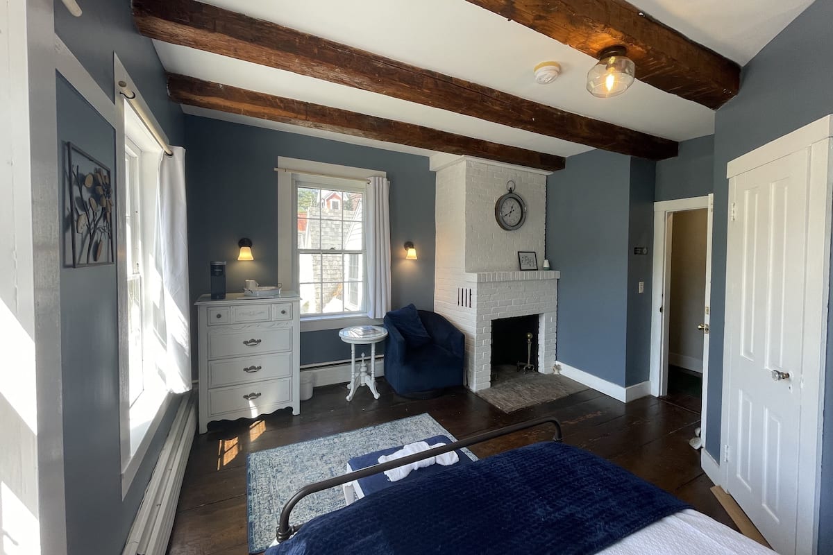 A bedroom with a bed, a fireplace, a window, a dresser, and a clock on the wall.