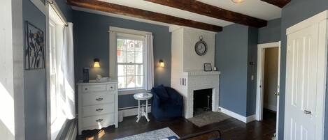 Une chambre à coucher avec un lit, une cheminée, une fenêtre, une commode et une horloge au mur.