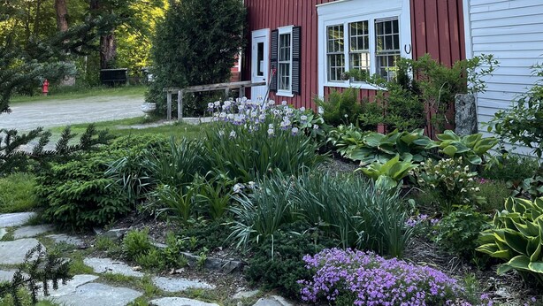 A red barn with a white door and shutters, surrounded by a garden with various plants and flowers. - Stone Hearth Inn and Eatery (Chester)