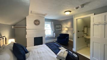 A bedroom with a bed, a chair, a clock, a window, and a door leading to a bathroom.