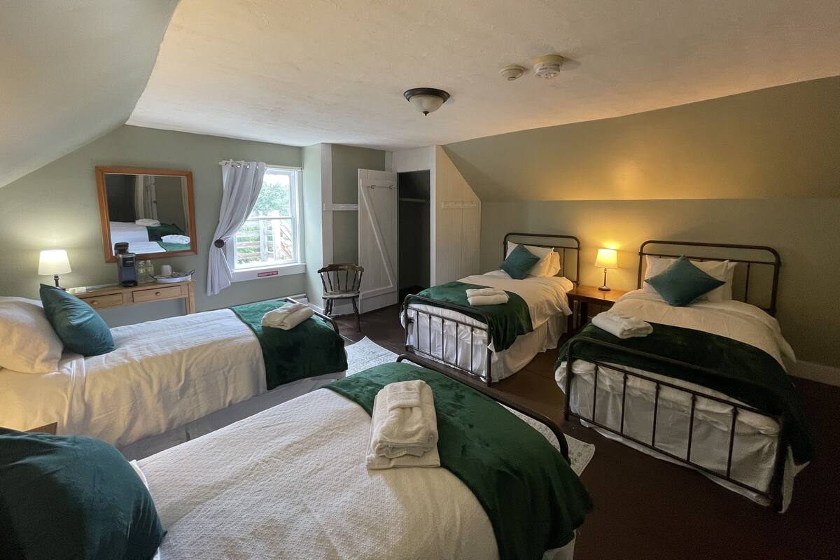 A hotel room with two single beds, a desk with a lamp, a chair, and a large window.