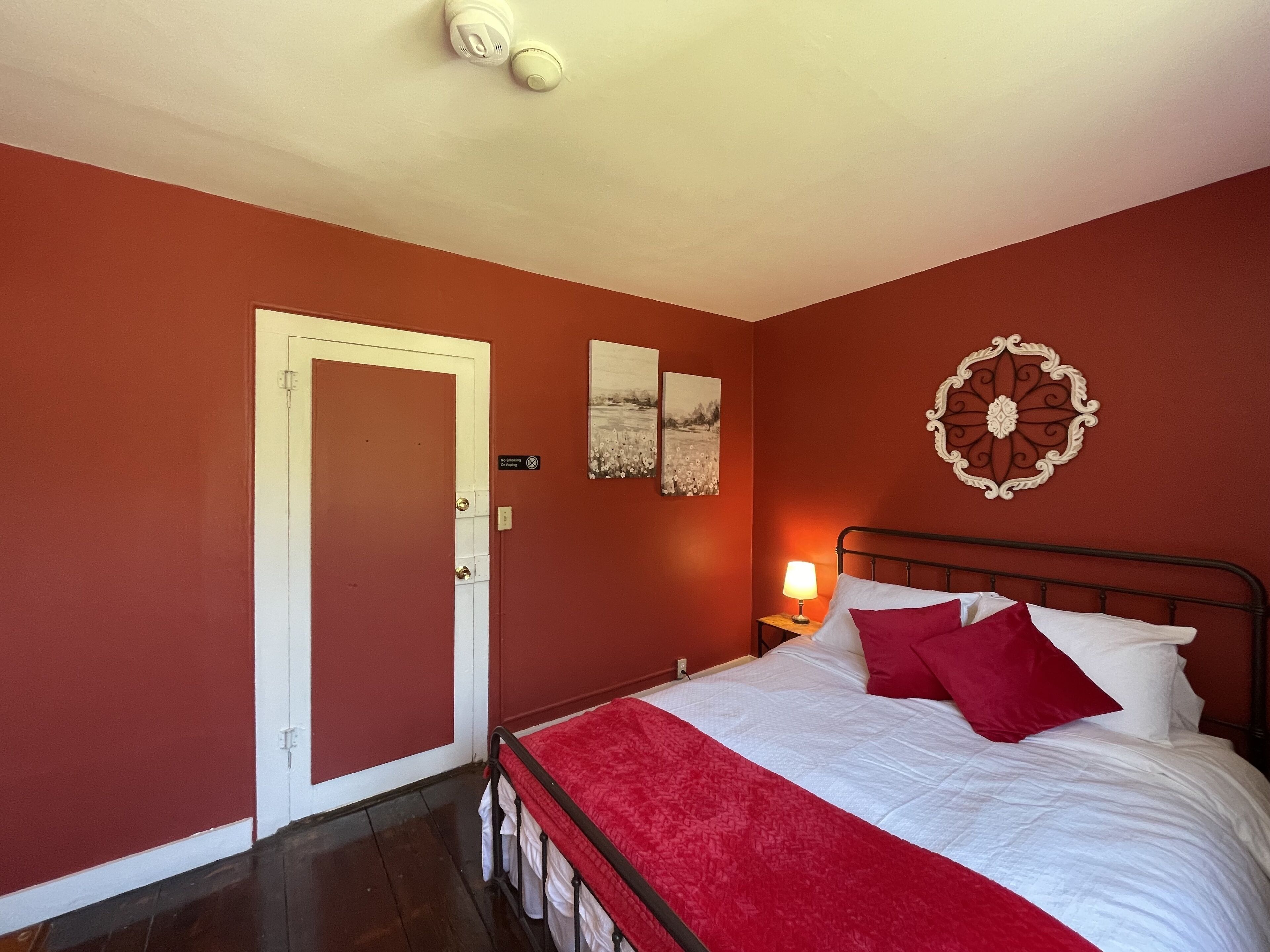 A bedroom with a bed, a nightstand, a lamp, a door, and two wall-mounted pictures.