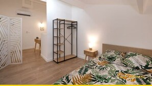 Ein Schlafzimmer mit einem Bett, einem Kleiderschrank, einem kleinen Tisch und einem an der Wand befestigten Regal.