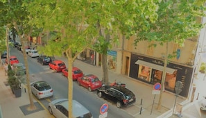 A street view with parked cars, trees lining the sidewalk, and storefronts including a visible 'VILLARD' sign.