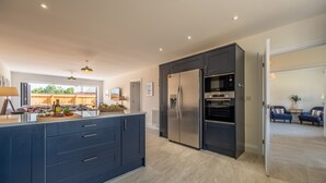 A modern kitchen with dark cabinetry, a central island, and a built-in oven. - Sandpiper House (4), Ingoldisthorpe, Norfolk (Ingoldisthorpe)