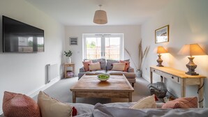 A living room with a sofa, a coffee table with a bowl, a TV, a window, and a lamp. - Sandpiper House (4), Ingoldisthorpe, Norfolk (Ingoldisthorpe)