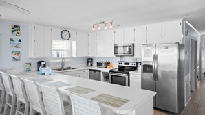 Una cucina moderna con mobili bianchi, elettrodomestici in acciaio inossidabile e un'isola centrale con sgabelli da bar.