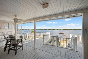 A covered deck with a view of the water, a chair, and a ceiling fan.