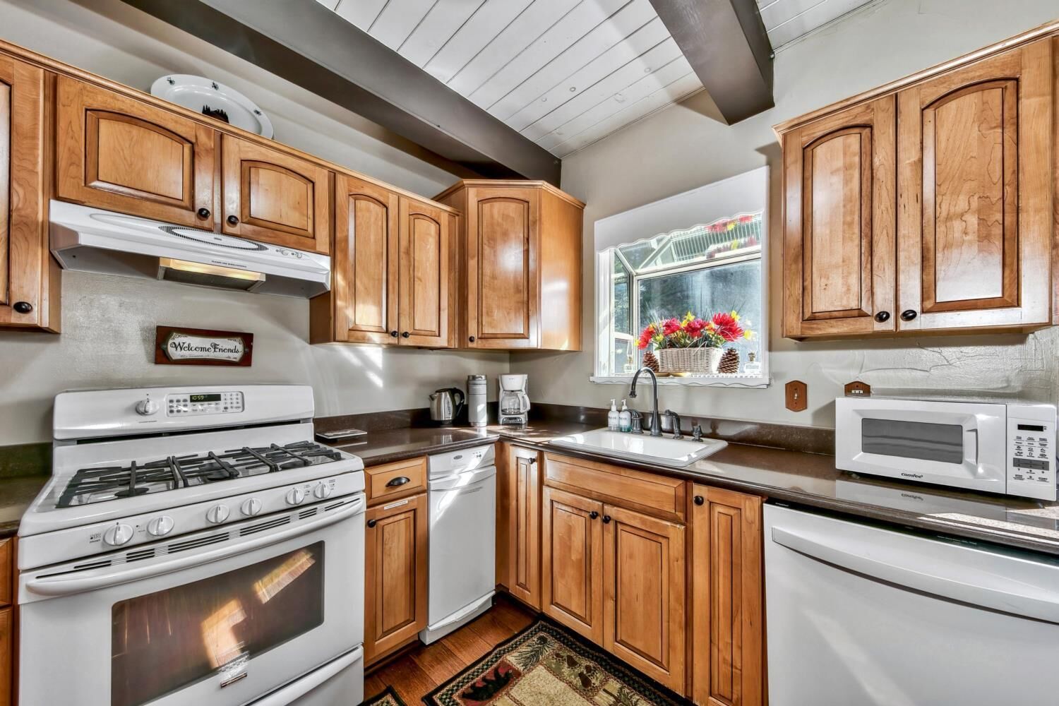 A kitchen with wooden cabinets, a stove, a microwave, and a window with flowers.