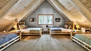 A cozy attic bedroom with two wooden beds, a window, and a small table.